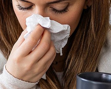 Symptome bei Sinusitis oder Schnupfen unterscheiden sich. Frau hat Schnupfen und schnäuzt in ein Taschentuch.